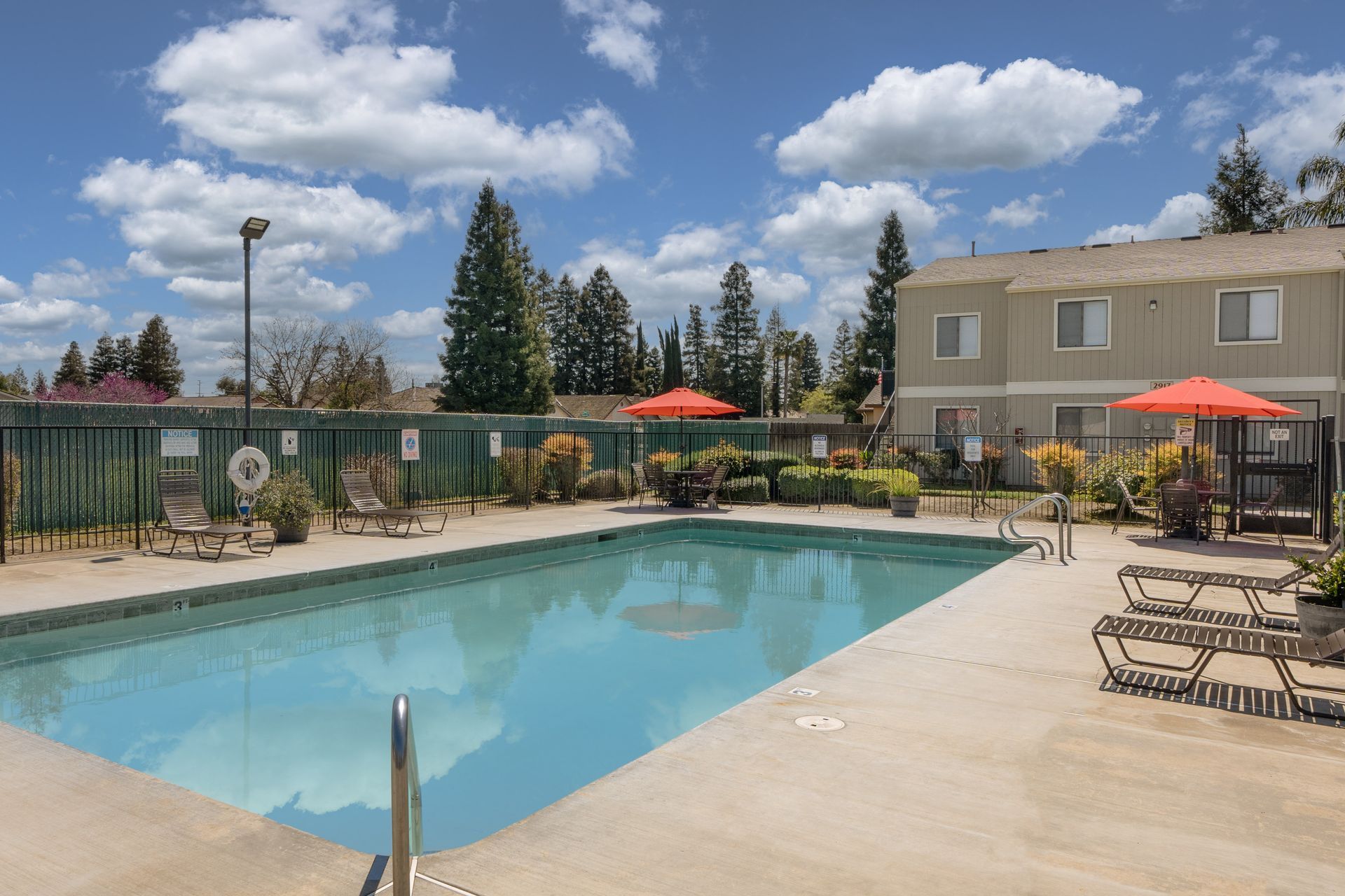 Swimming pool area with lounge chairs, umbrellas, and a building under a blue sky.