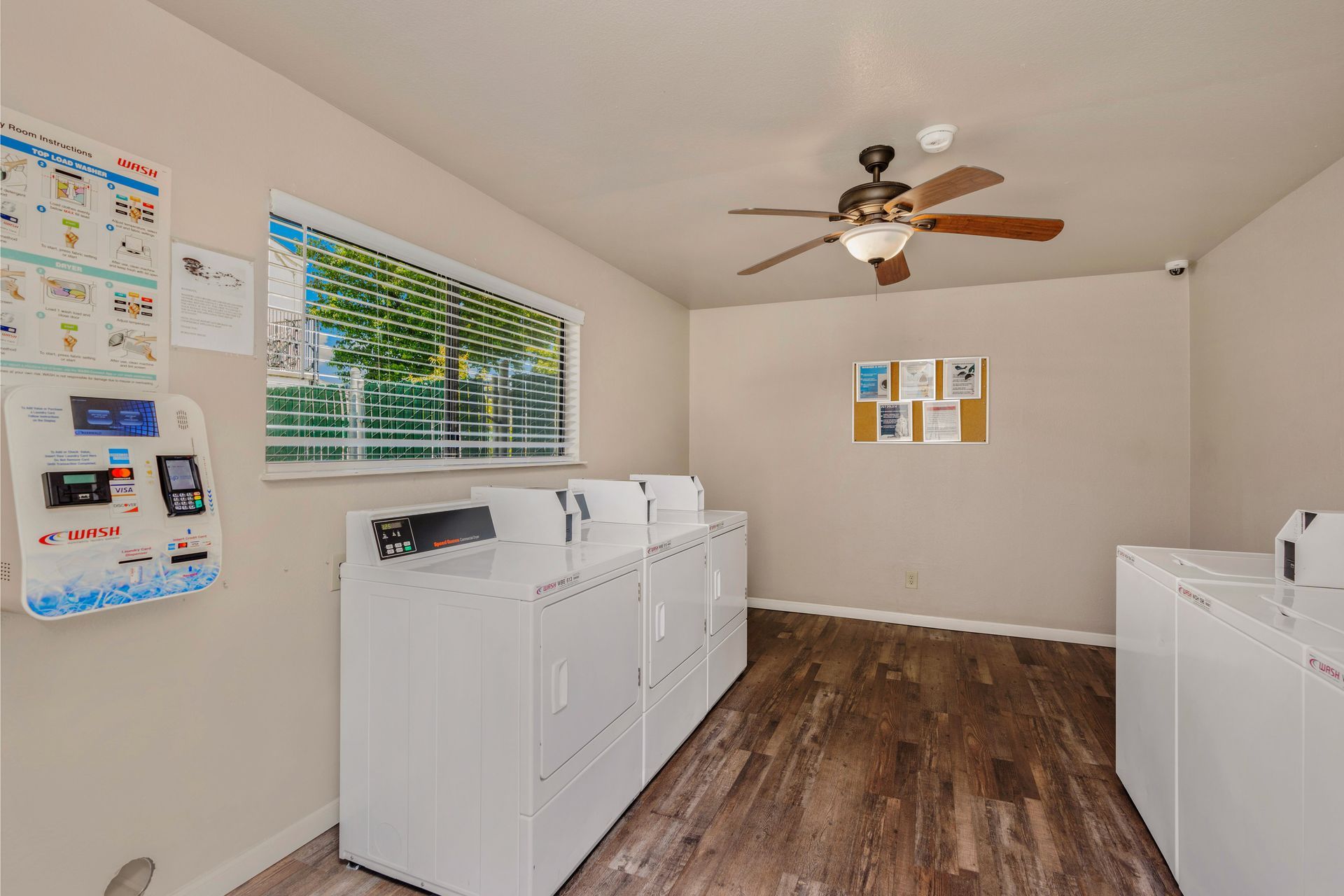 Laundry room with washers, dryers, and a pay station. Sunlight streams through a window.