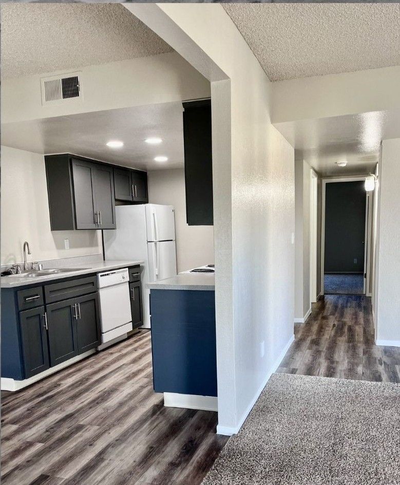Kitchen with dark gray cabinets, white appliances, and a hallway with a dark gray door.