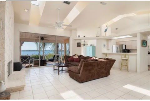 Picture of a spacious living room with white tile floor overlooking palm trees and the ocean.