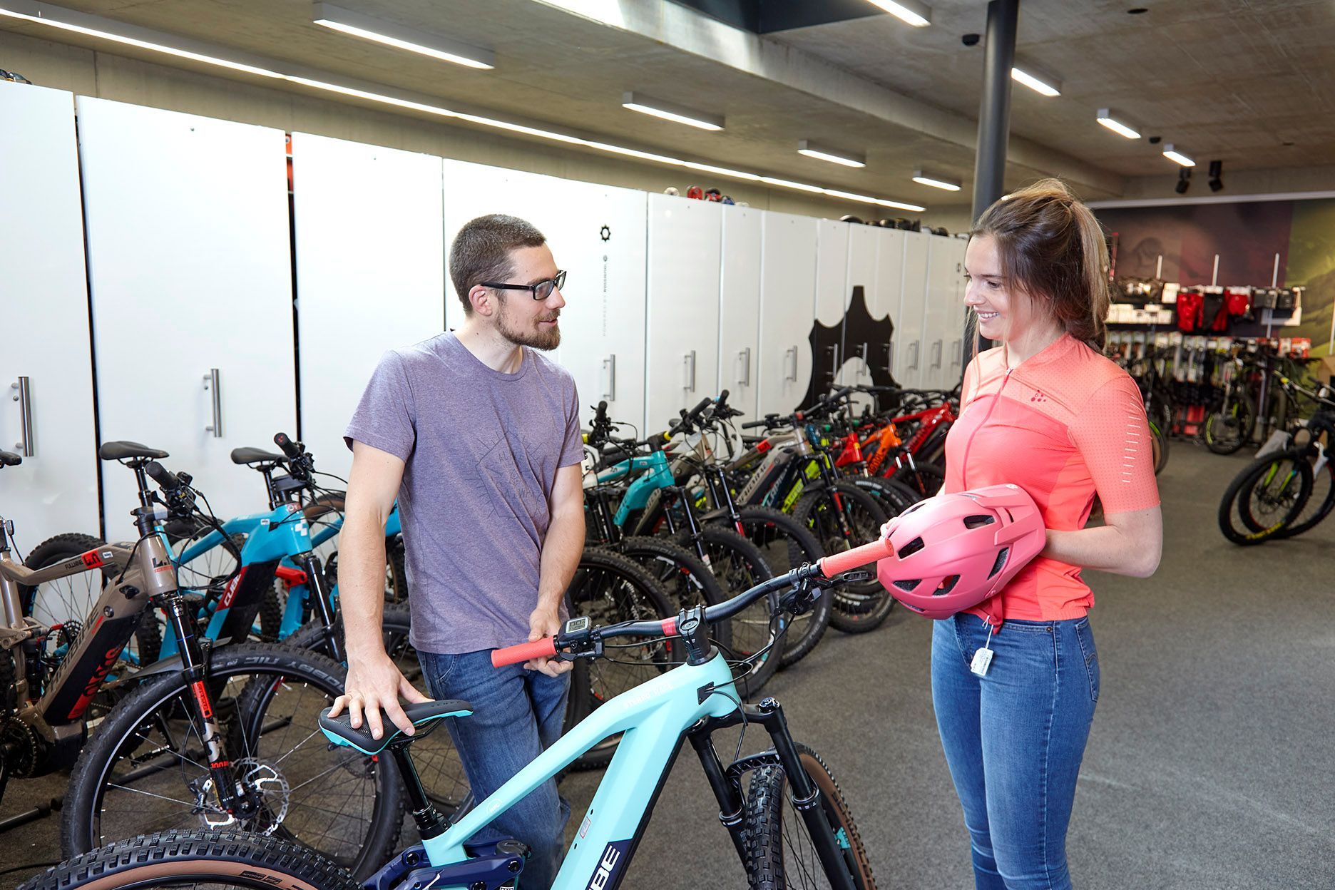 Zwei Personen unterhalten sich neben Fahrrädern in einem Fahrradladen, eine von ihnen hält einen pinkfarbenen Helm in der Hand.