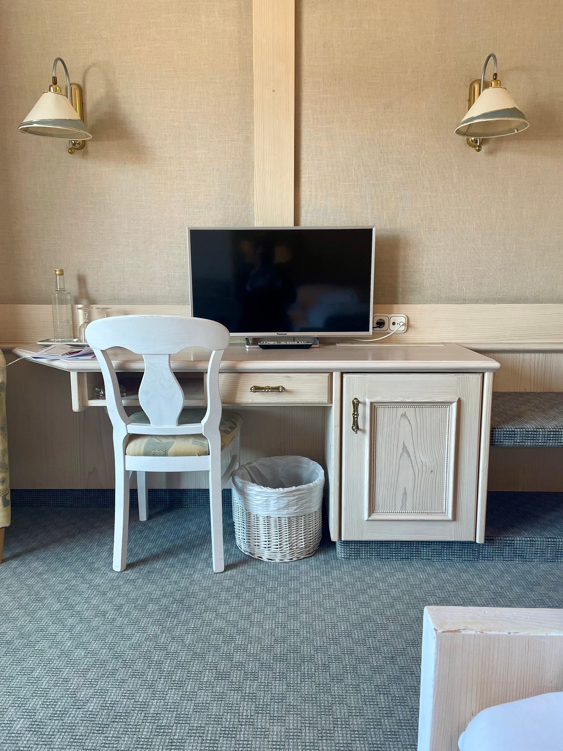 Ein Hotelzimmer mit Schreibtisch, Stuhl, Fernseher und Mülleimer.