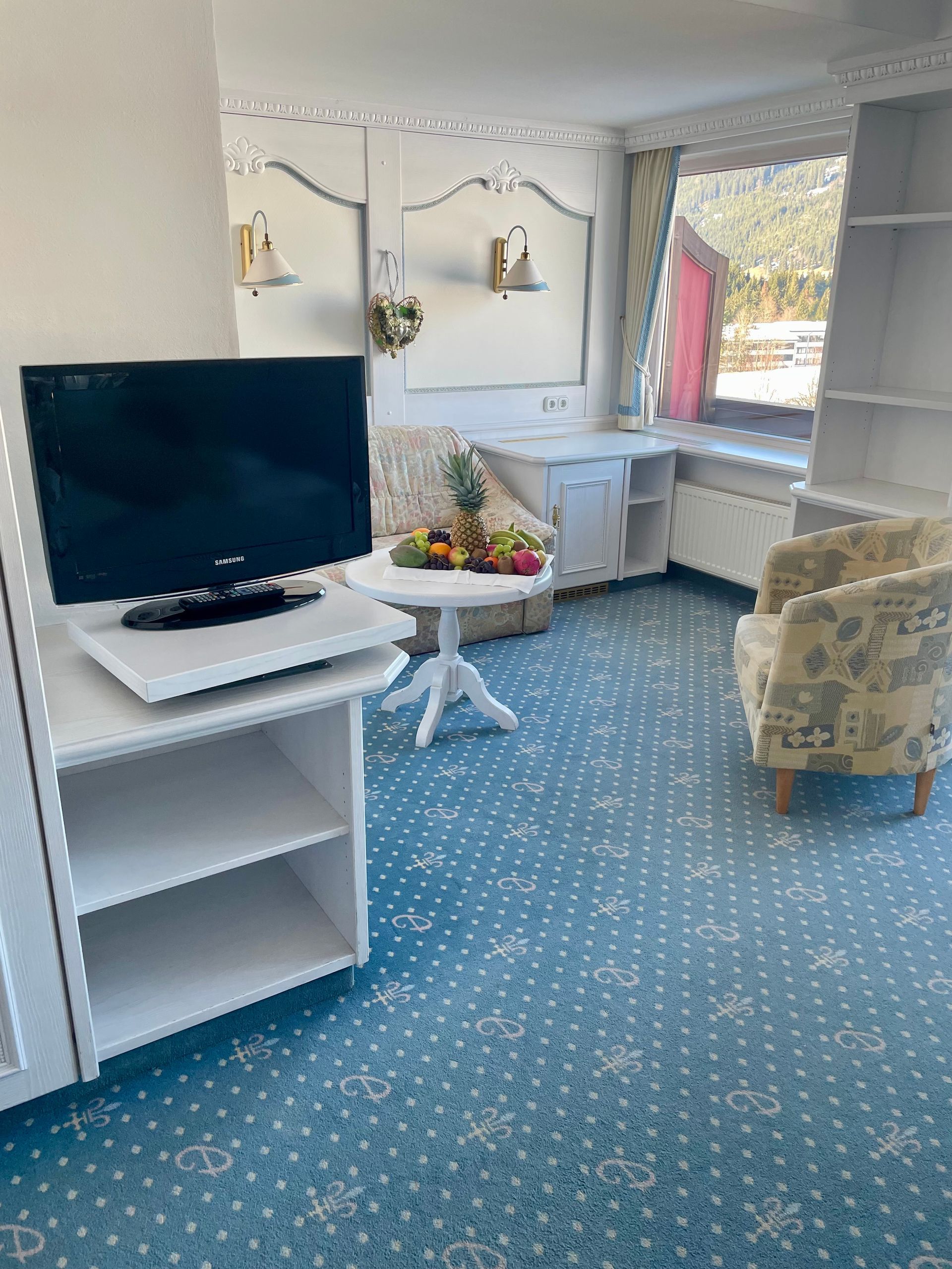 Ein Wohnzimmer mit Fernseher, Stuhl, Tisch und Fenster.