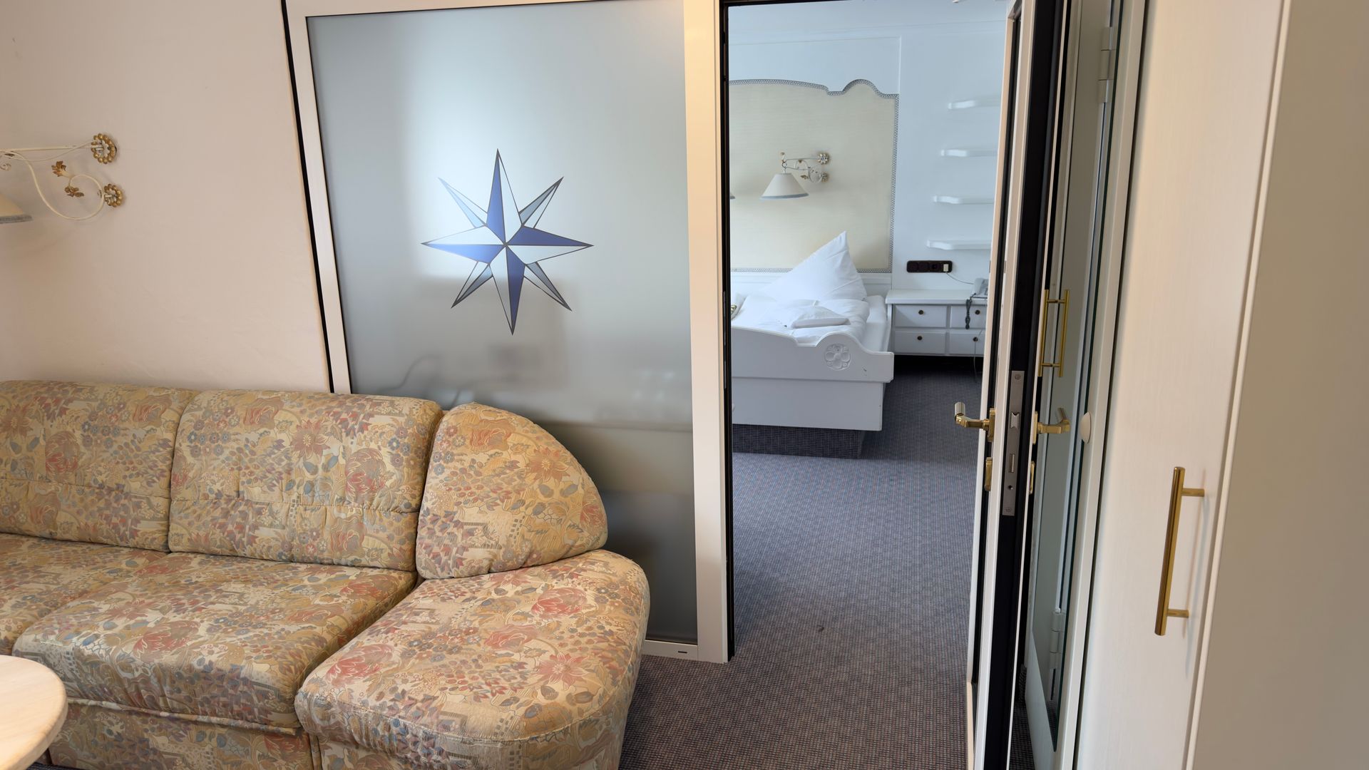 Ein Wohnzimmer mit Couch und Sessel und eine Glasschiebetür, die zu einem Schlafzimmer führt.