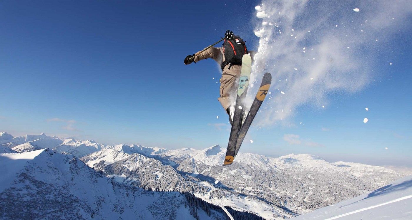 Eine Person springt in die Luft, während sie einen schneebedeckten Berg hinunterfährt.