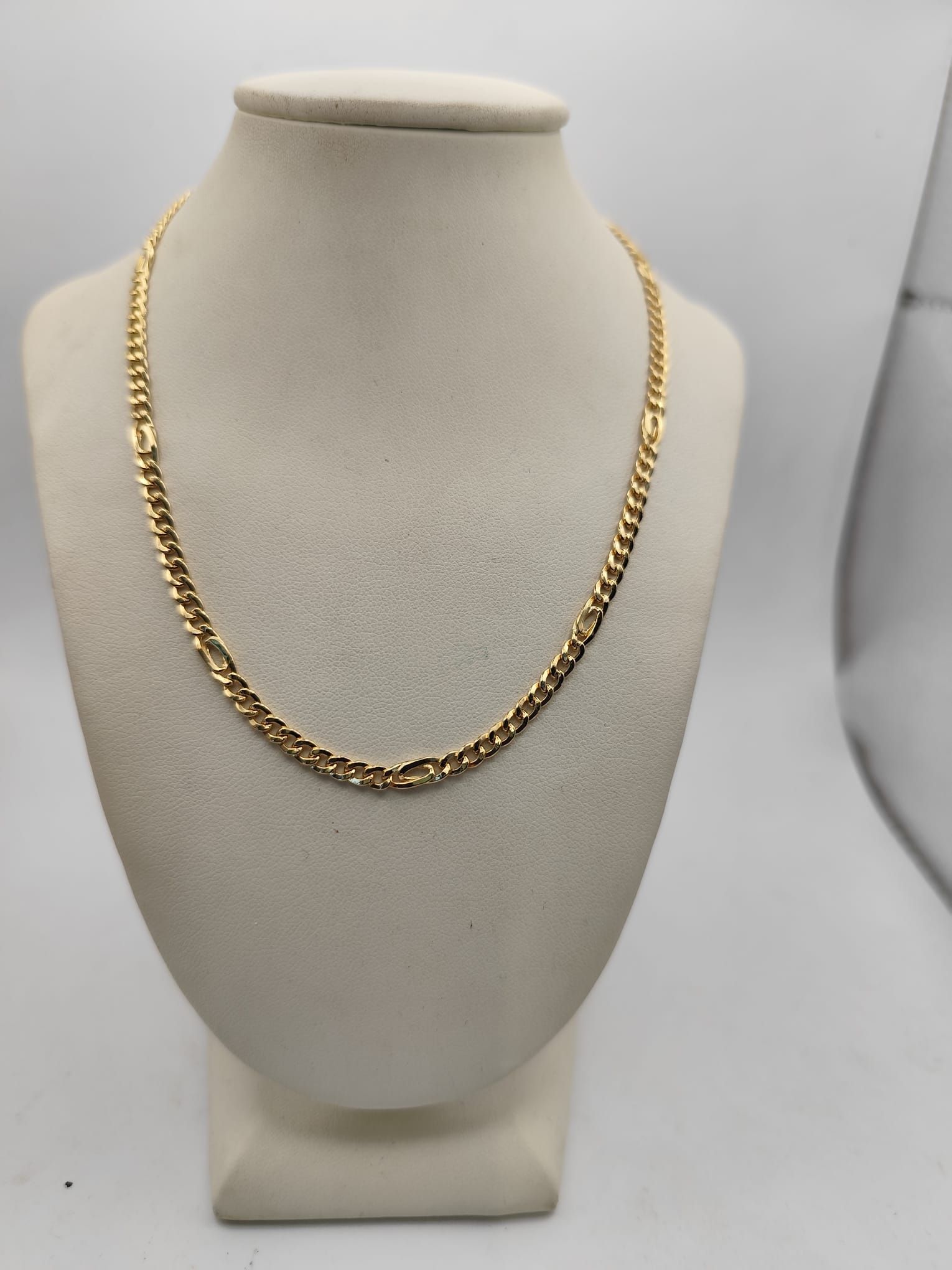 Collana con catena d'oro esposta su un busto portagioie color crema su sfondo bianco.