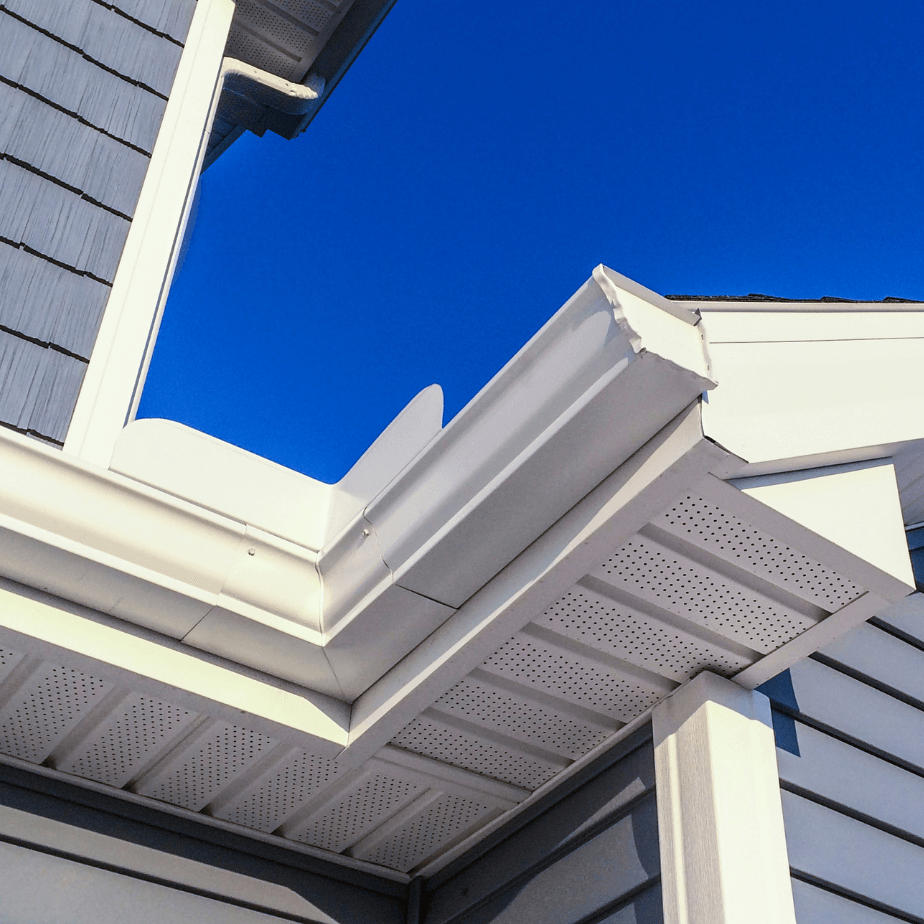 White house eaves and roofline with siding against a bright blue sky