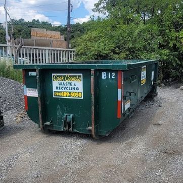 Green dumpster filled with construction debris, beside a building under construction.