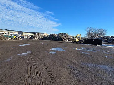 A construction site with piles of debris, an excavator, and a building under a blue sky.