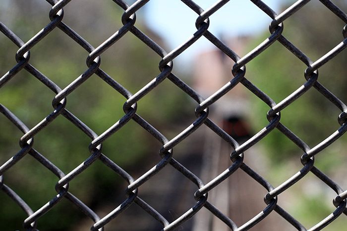 Chain-link fence in focus with a blurred person and buildings in the background