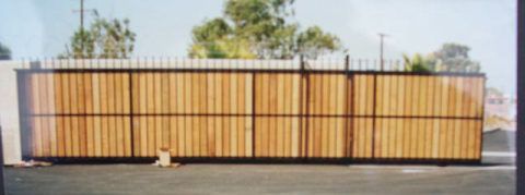 Long wooden fence with a black metal frame beside a road under a clear sky