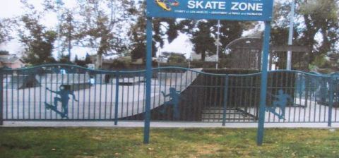 Outdoor skate zone with empty concrete bowl, blue sign, and fenced entrance
