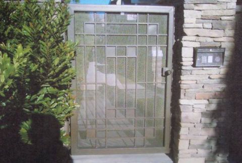 Metal security gate at a stone house entrance with a wall-mounted intercom keypad nearby