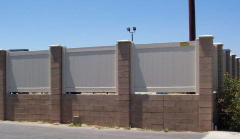 Brick wall with tall light gray fence panels and a utility pole beside a sidewalk