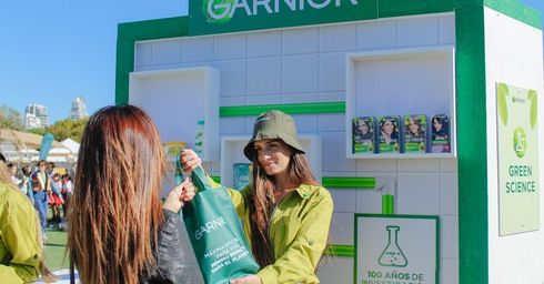 Woman in green shirt gives a Garnier bag to another woman at an outdoor Garnier event.