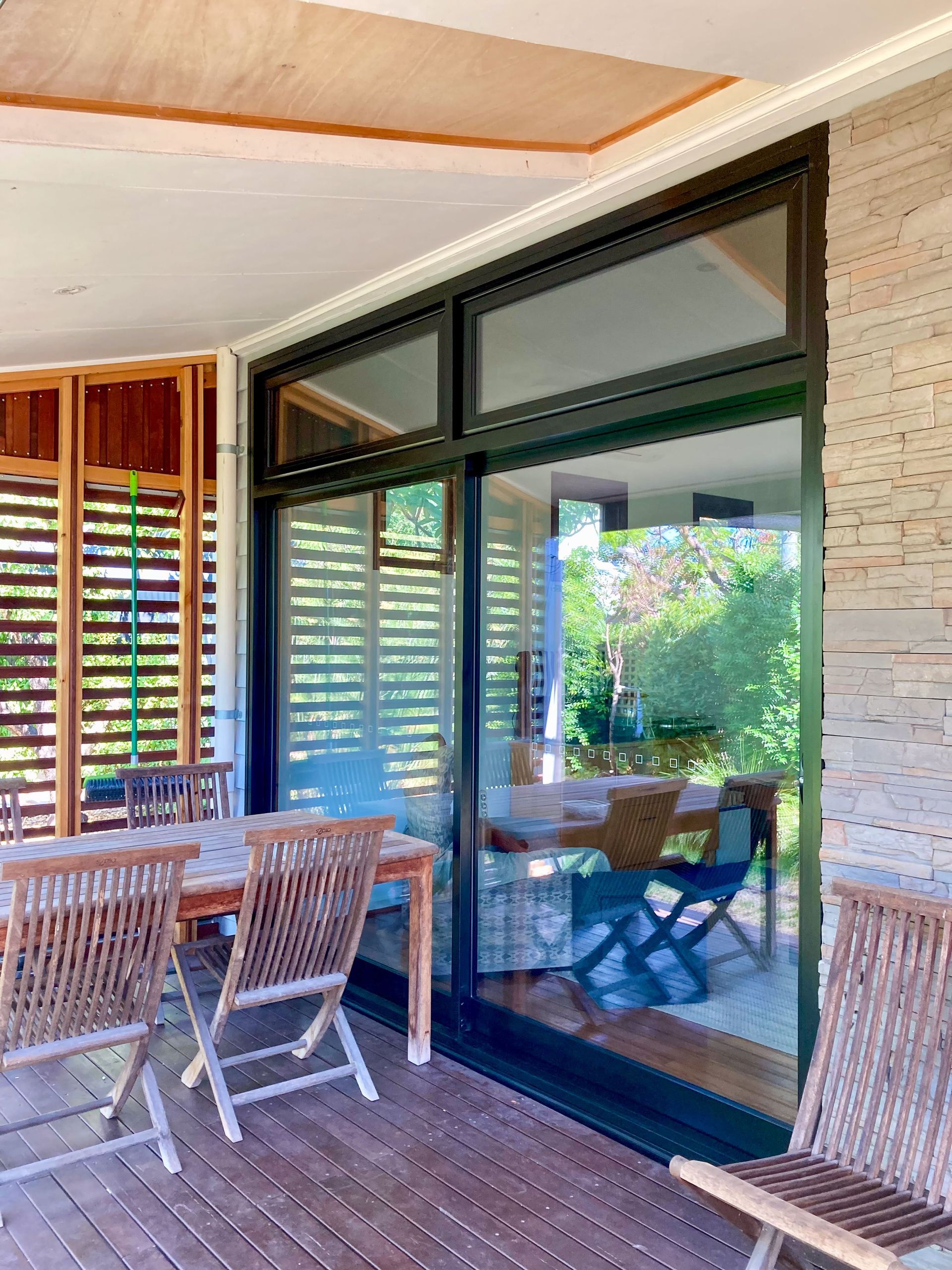 Patio with sliding glass door, wooden deck, table, chairs, and view of greenery.