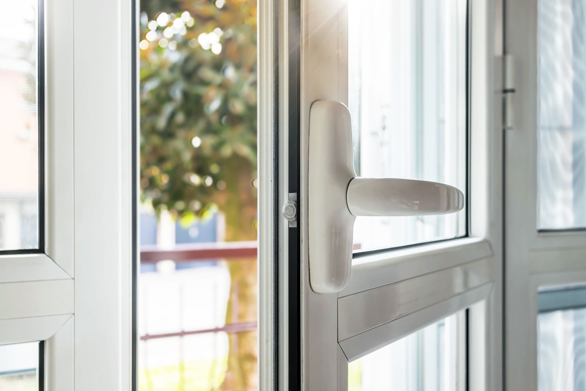 A WHITE DOUBLE-GLAZED DOOR WITH A HANDLE WITH A VIEW OUTDOORS OF A TREE.