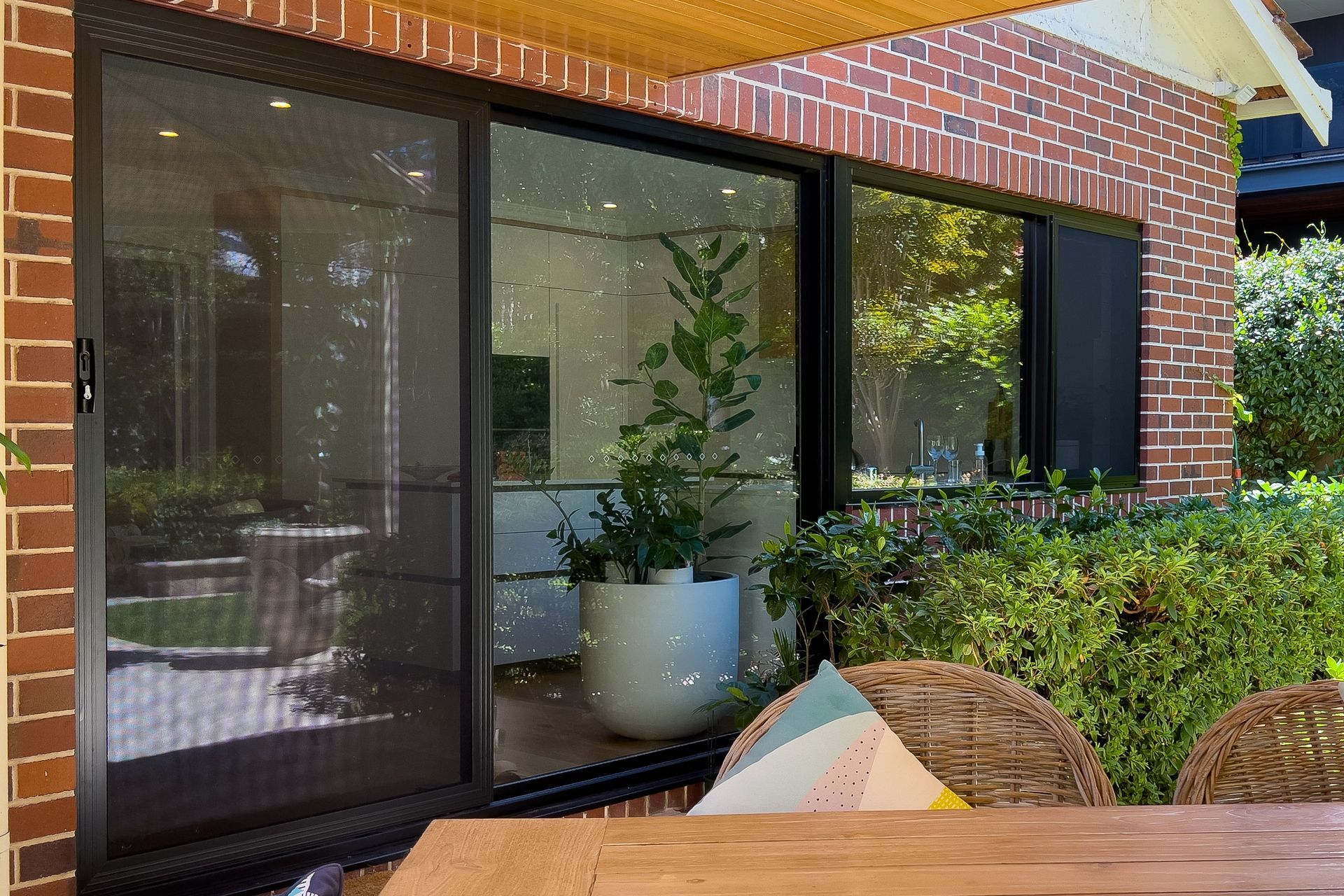 Sliding glass door with black frame, next to red brick wall and plants.