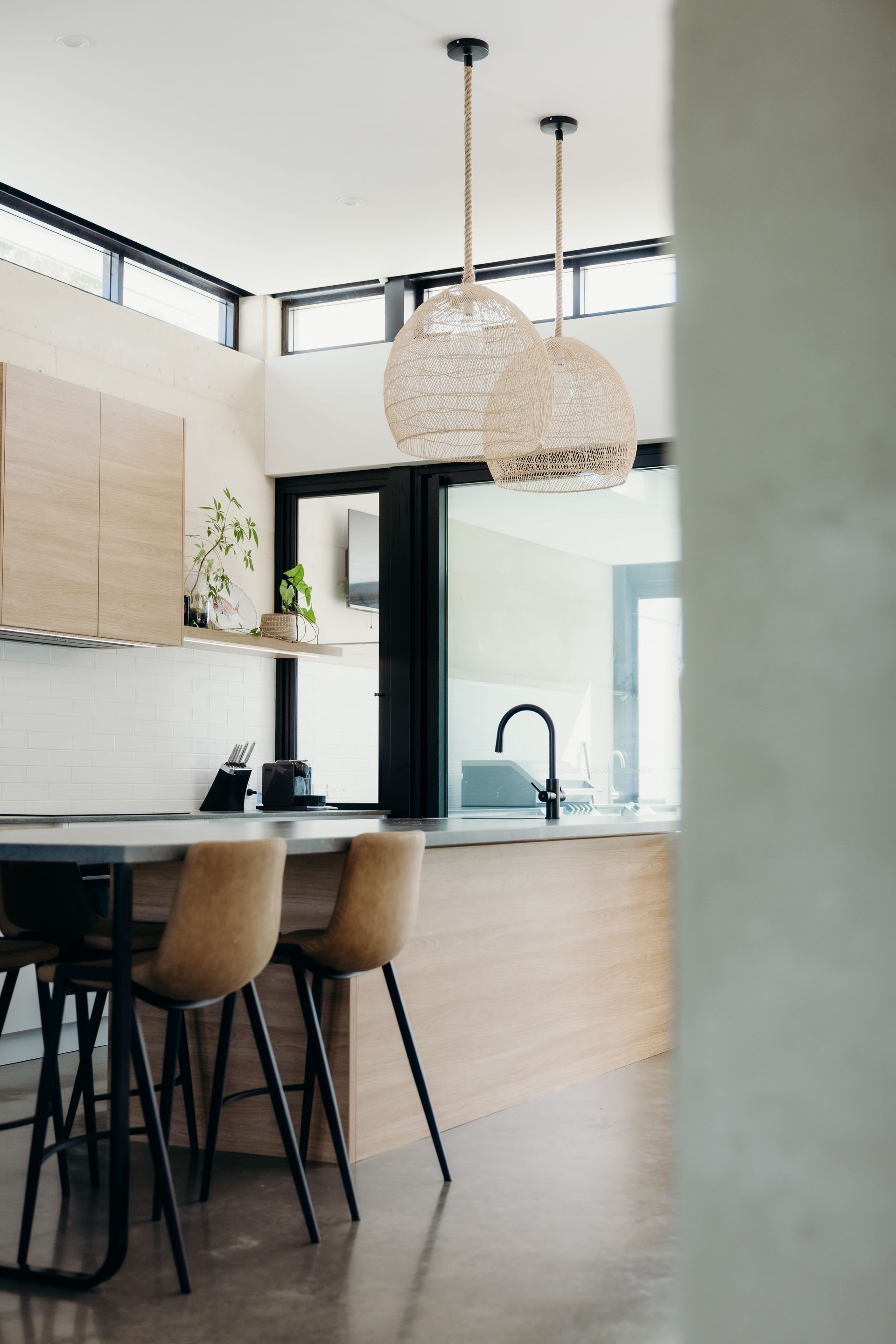Modern kitchen with woven pendant lights, bar stools, and large windows.