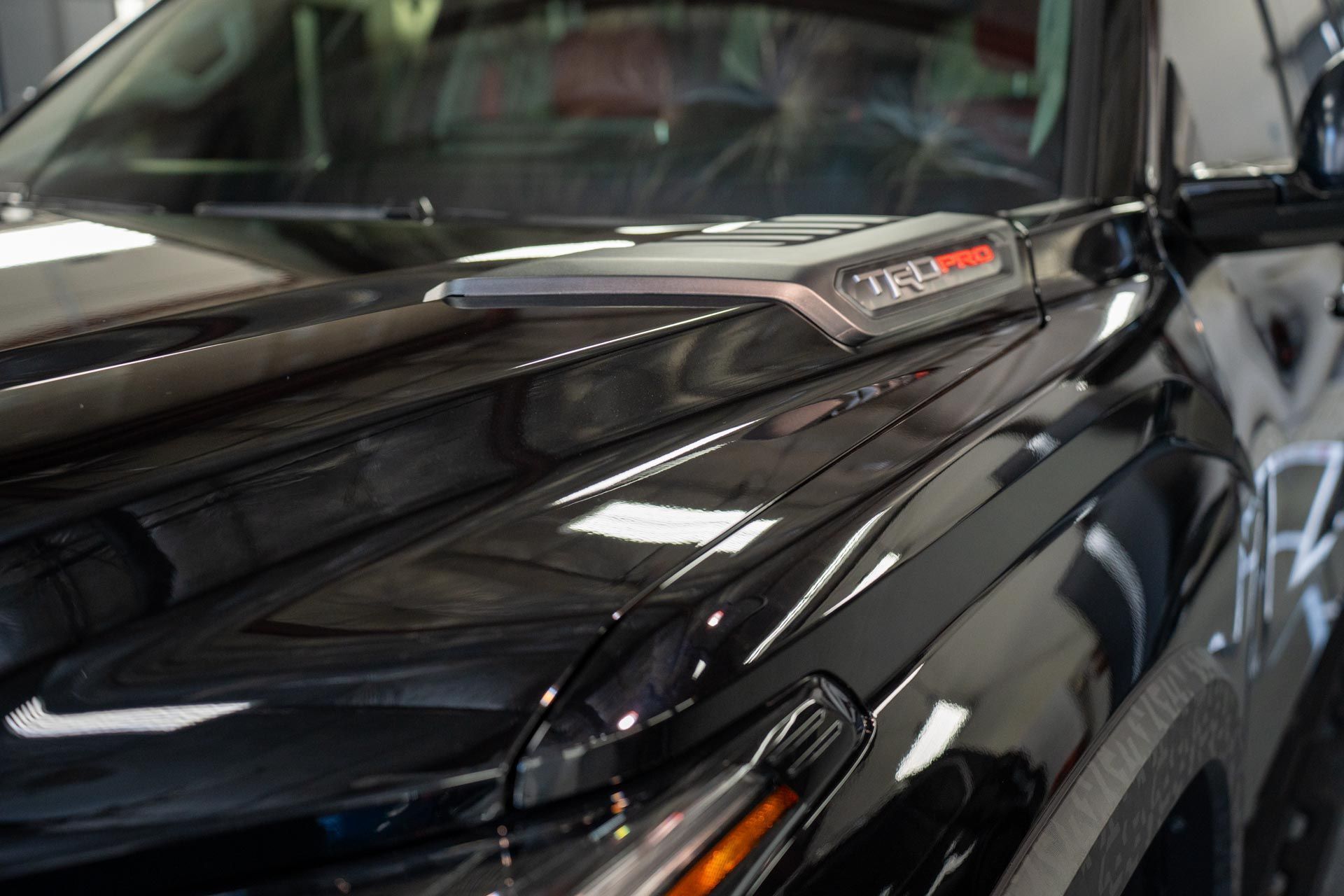 Black vehicle hood with a TRD Pro hood scoop, close-up. Shiny paint reflects light.