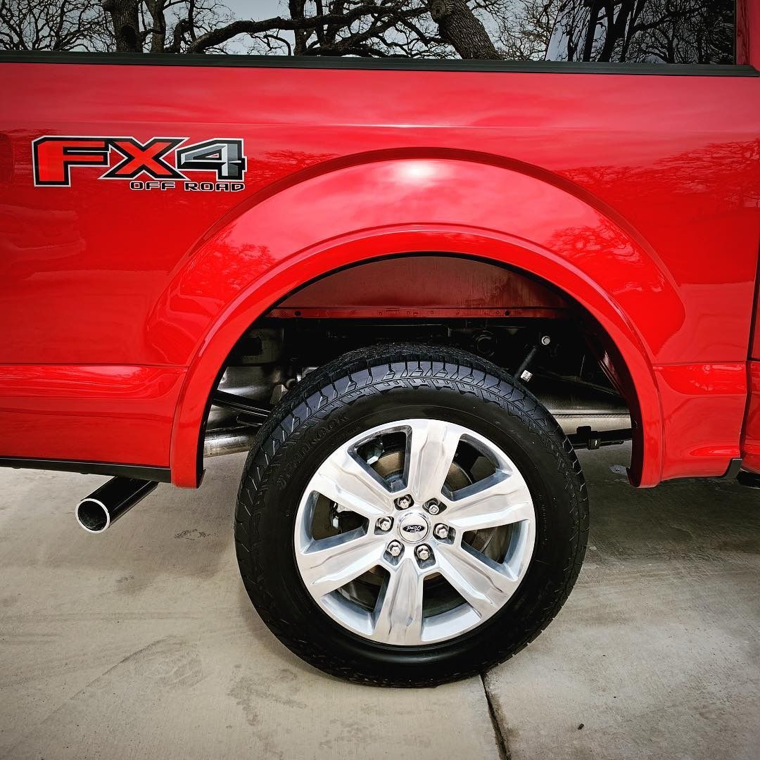 Red Ford F-150 truck's rear wheel and fender with FX4 logo. Chrome wheel, black tire, and exhaust pipe are visible.