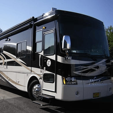 Black and cream RV parked outdoors. Shows front and side.