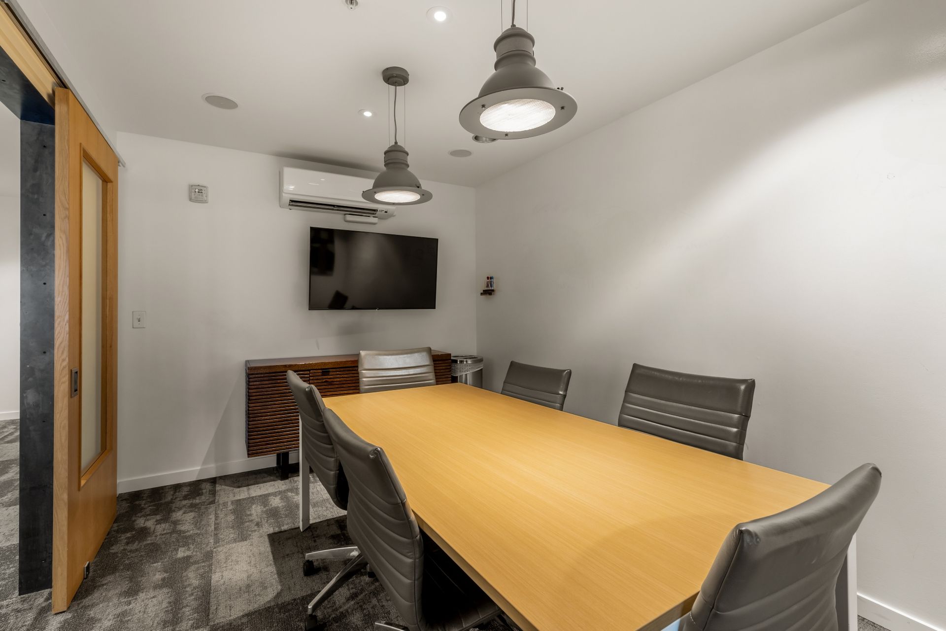 A conference room with a long wooden table and chairs and a flat screen tv.