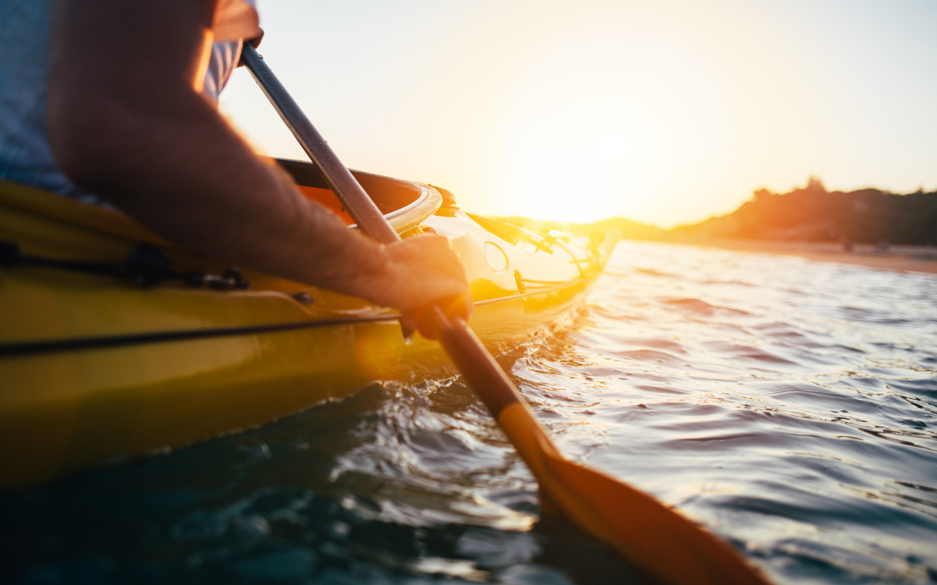 A man is paddling a kayak on a lake at sunset.
