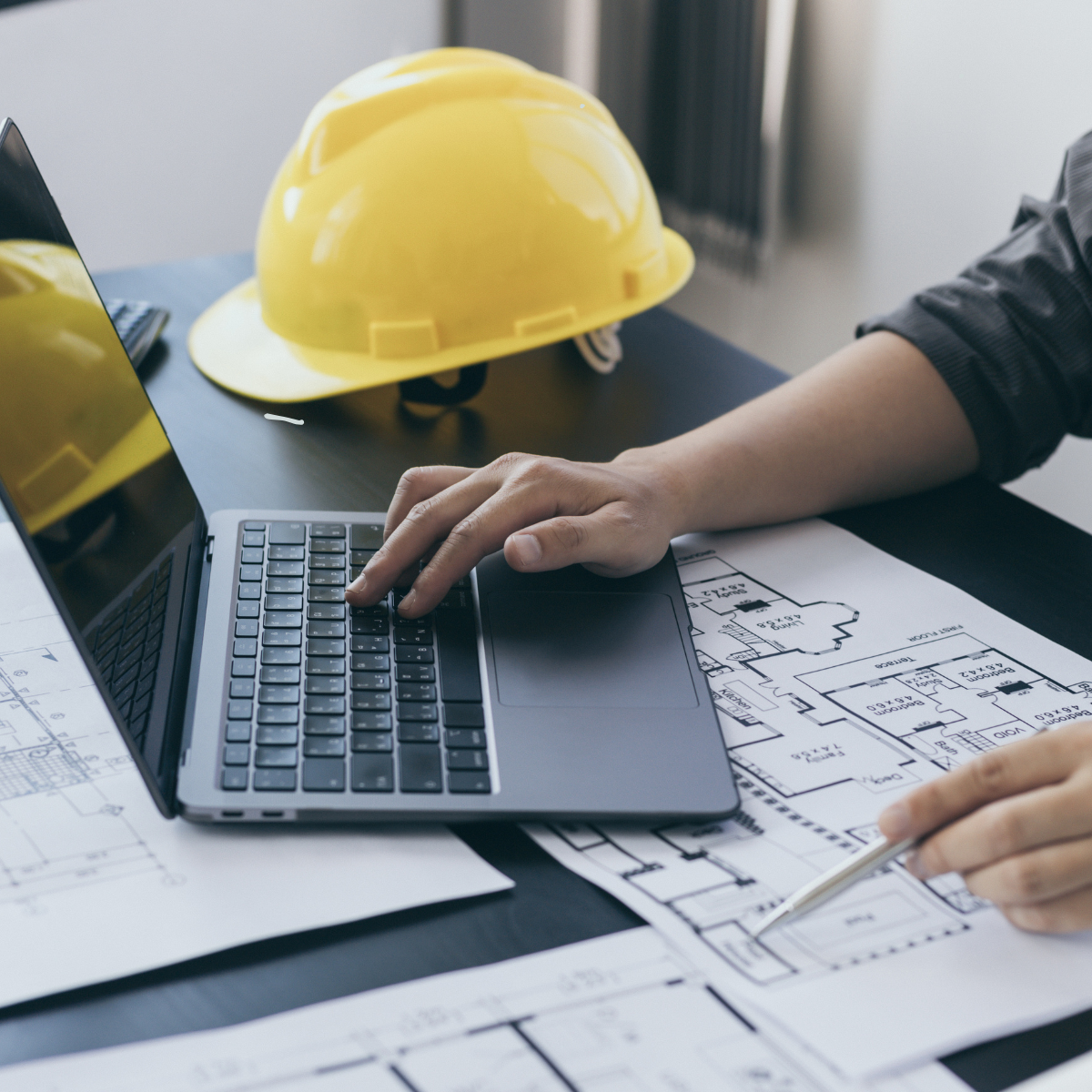 Person writing at a computer with a construction worker helmet on the desk