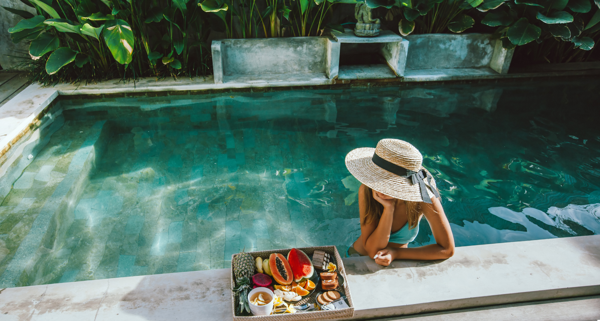 Woman in a swimming pool with a hat and exotic fruit platter