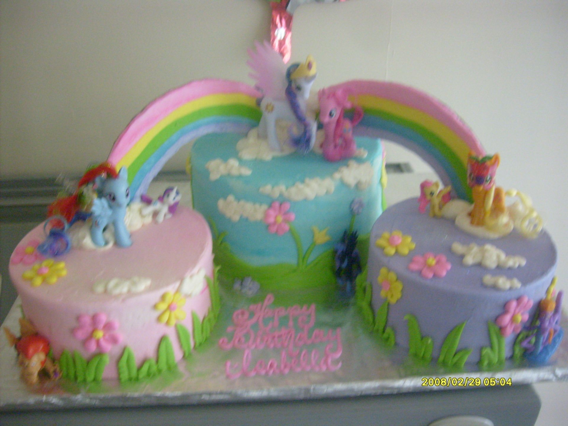 Colorful unicorn birthday cake with rainbows, clouds, flowers, and three tiers on a table
