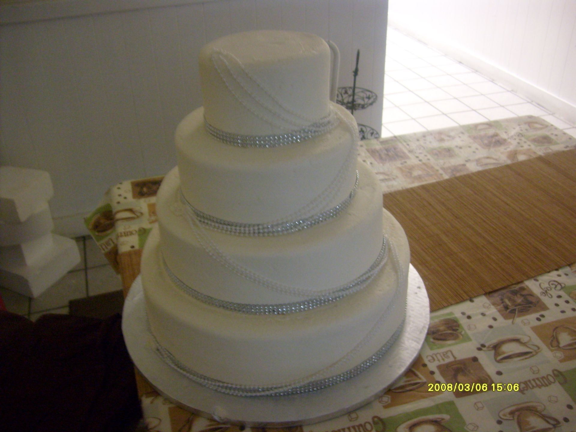 Four-tier white wedding cake with silver ribbon trim on a table indoors