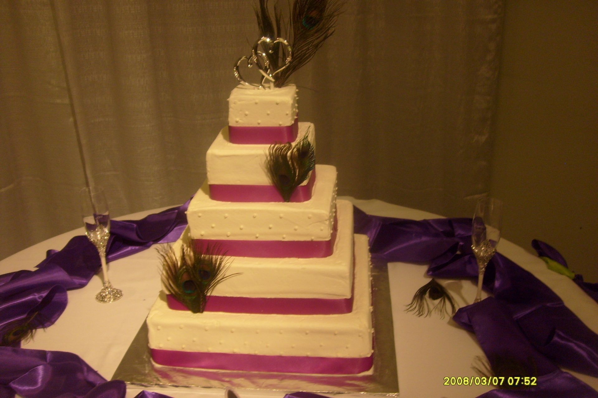 Three-tier white and purple cake centerpiece on a decorated table with purple drapes and gold accents