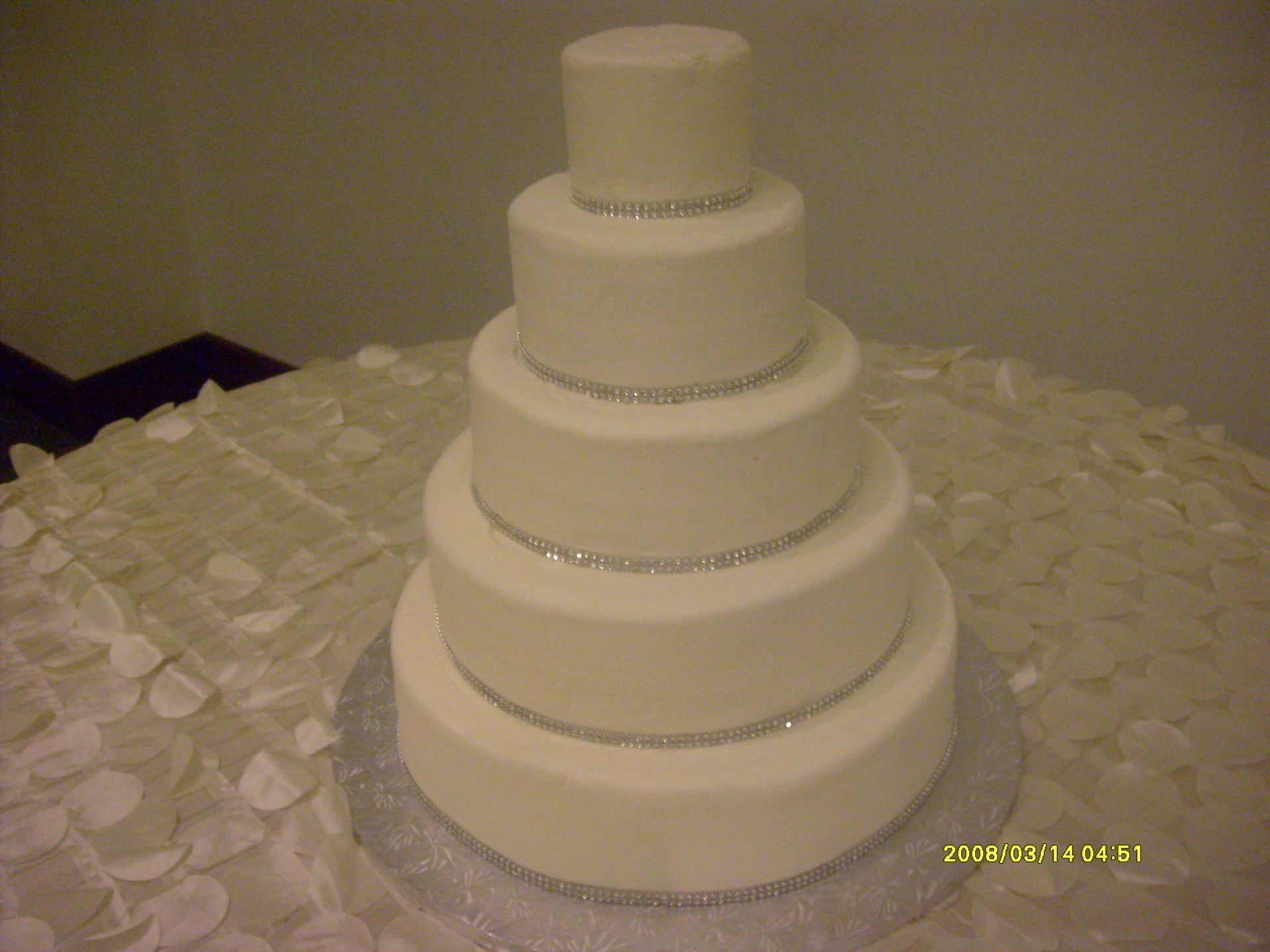 Four-tier white wedding cake on a table with a lace-like patterned cloth.