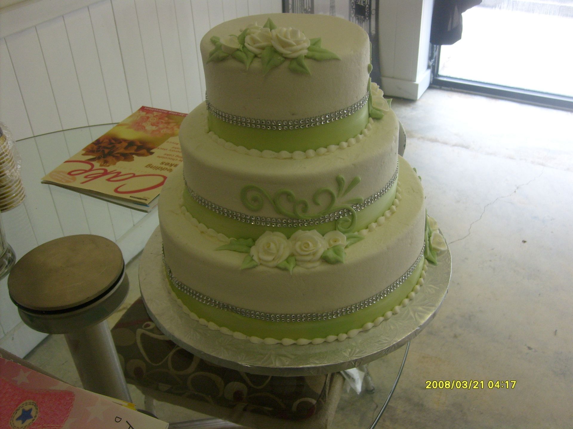 Three-tier white and green wedding cake with floral decorations on a table indoors