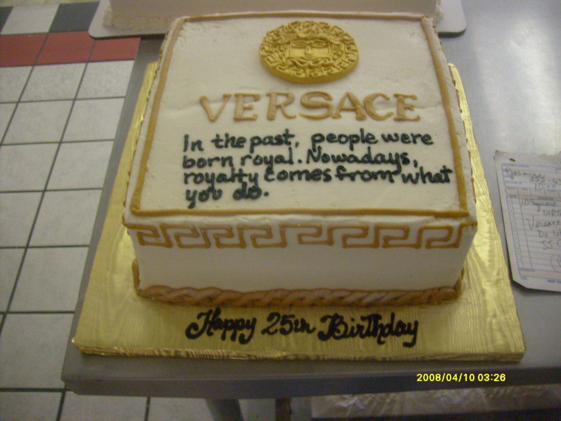 Versace birthday cake with gold trim and chocolate writing on a table