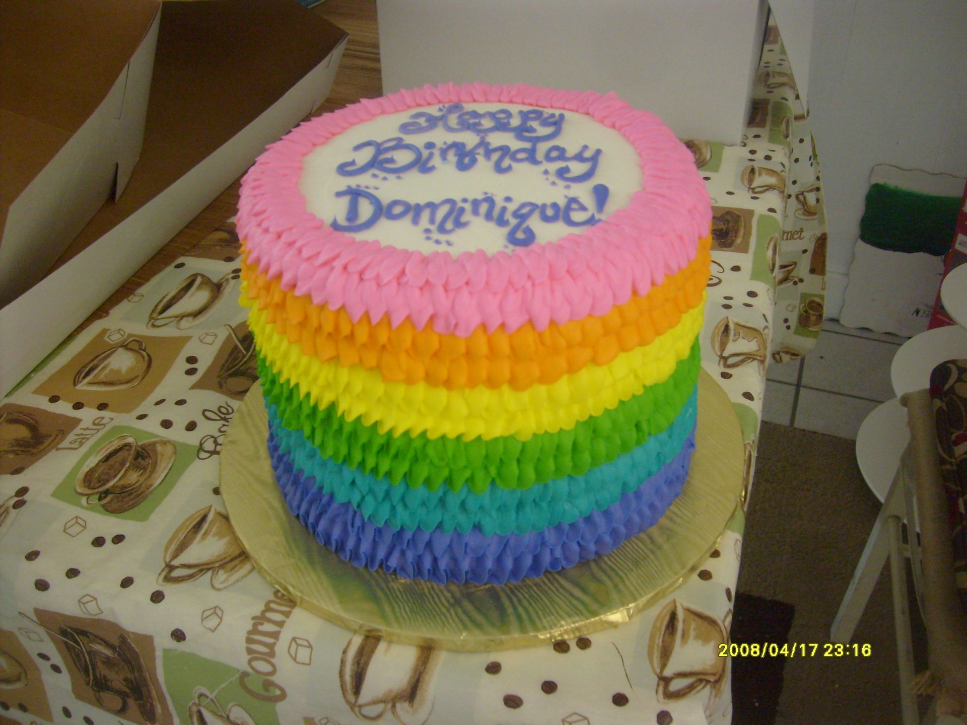 Rainbow-frosted birthday cake with “Happy Birthday Dominique” written on top in a box