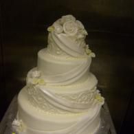 Tiered white wedding cake with floral decorations and ribbon-like frosting accents