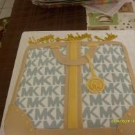 Gray-and-gold monogrammed gift bag with gold ribbon and circular logo on a table