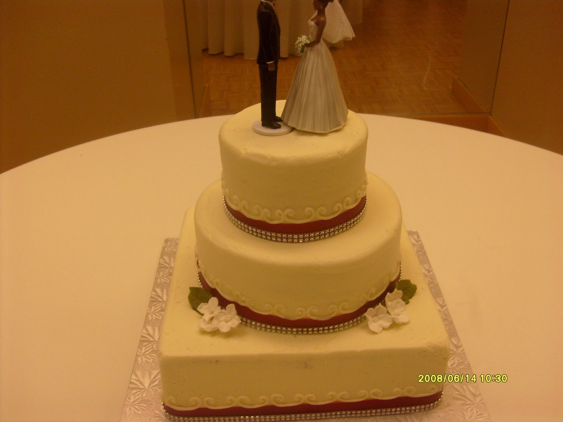 Three-tier white wedding cake with bride and groom topper on a round table