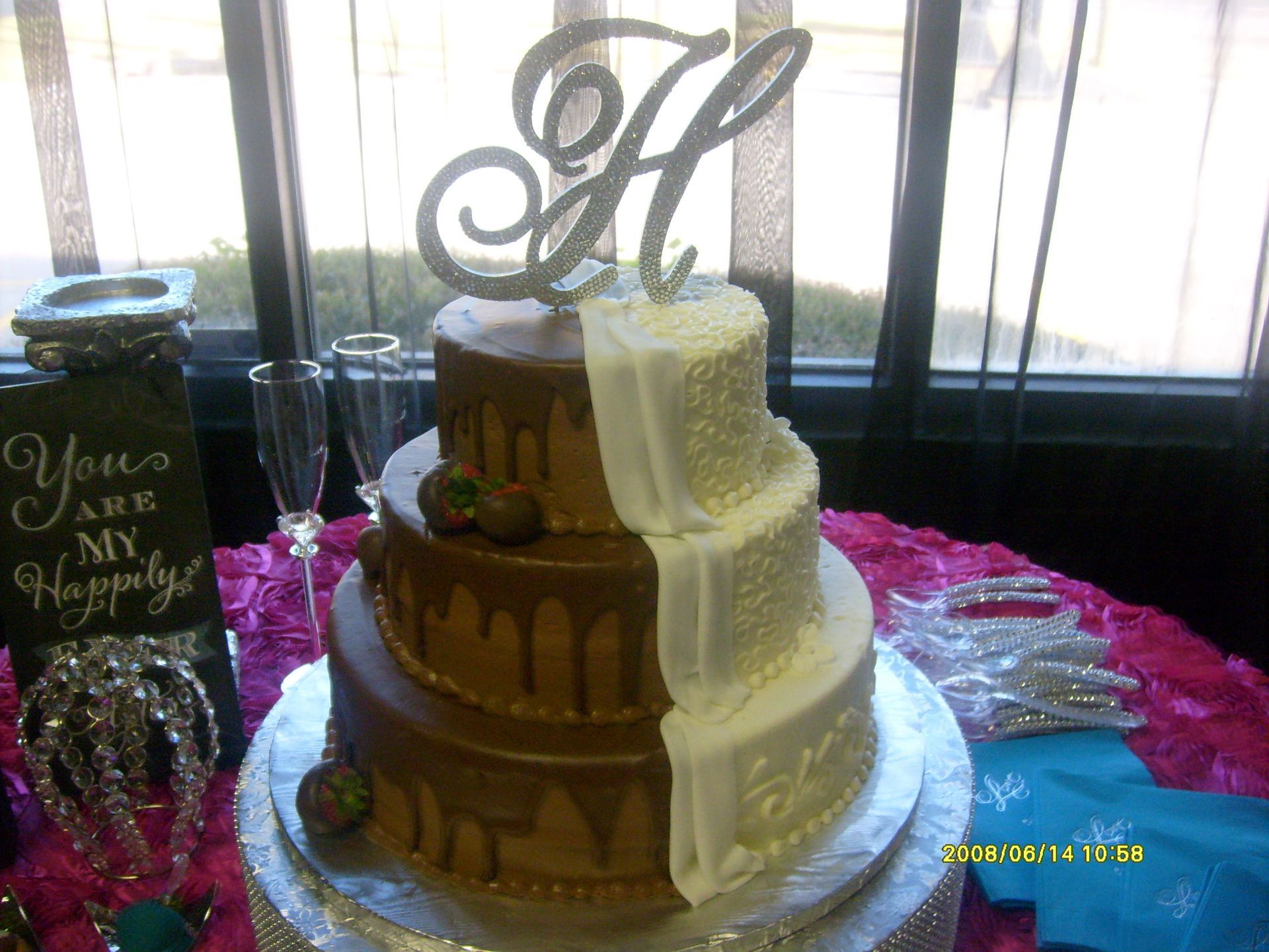 Two-tier gold-and-white wedding cake with monogram topper on a decorated table