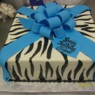 Square gift box wrapped in black-and-white zebra print with a large blue bow and ribbon