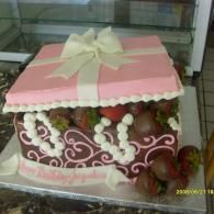 Pink and white gift box-shaped cake with a cream ribbon bow and floral decorations in a display case