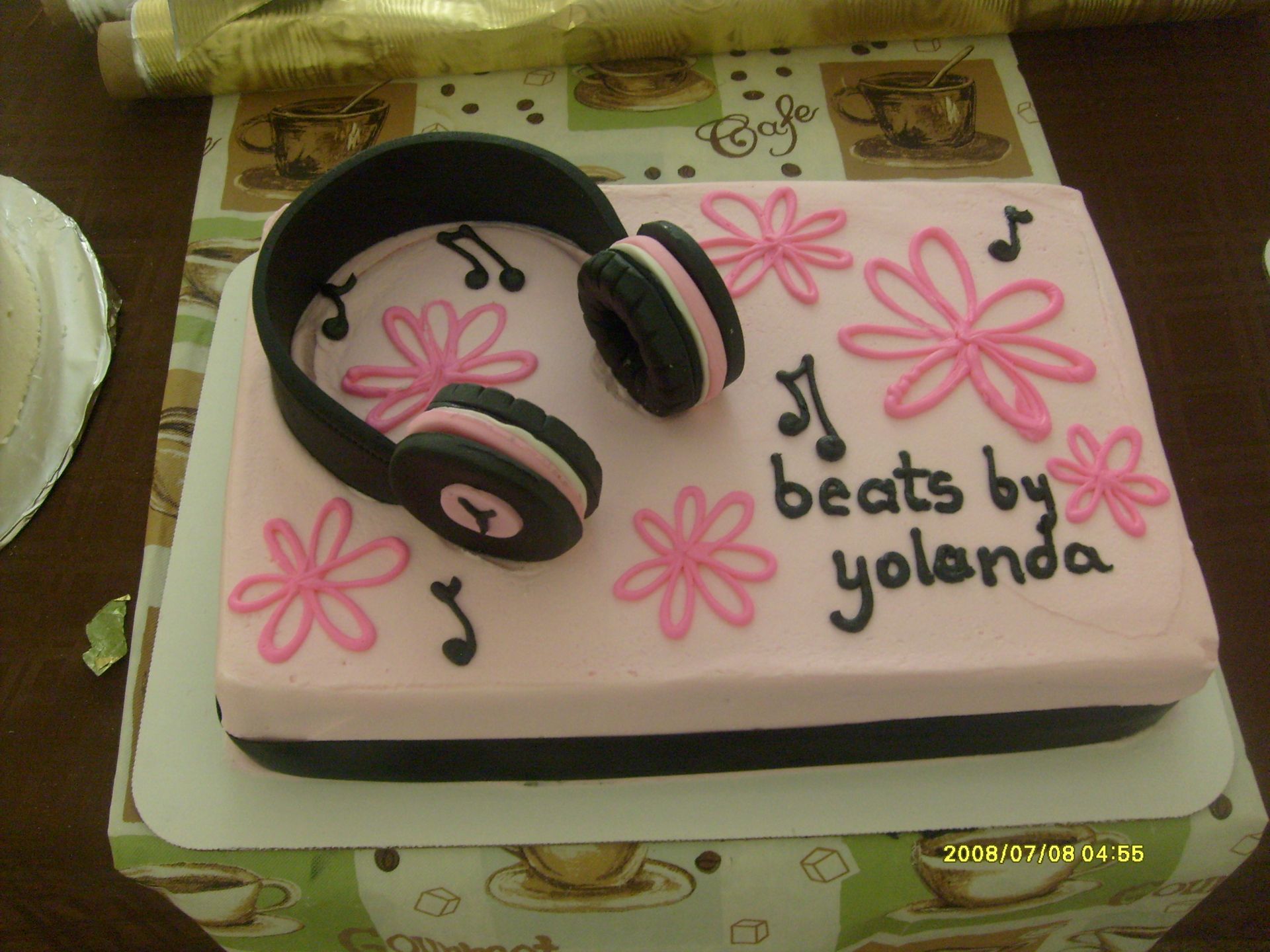 Pink cake decorated with black headphones, flowers, and “beats by yolanda” text