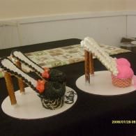 Two decorative arched cake sculptures on white plates, one black and white, one pink, on a table