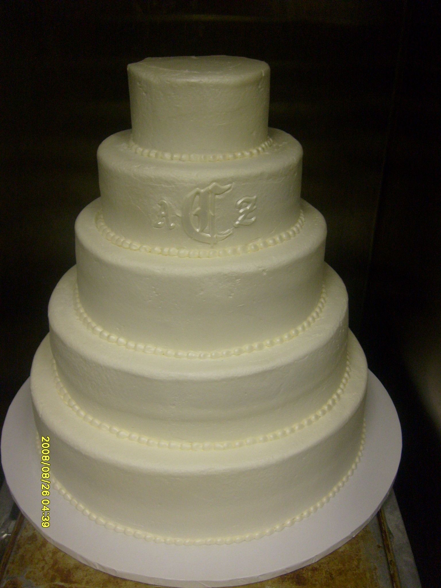 White tiered fondant wedding cake with pearl-like trim on a silver cake board