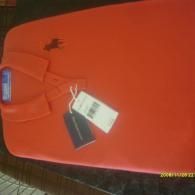 Orange handbag with tags and a small black item on top, lying on a red surface