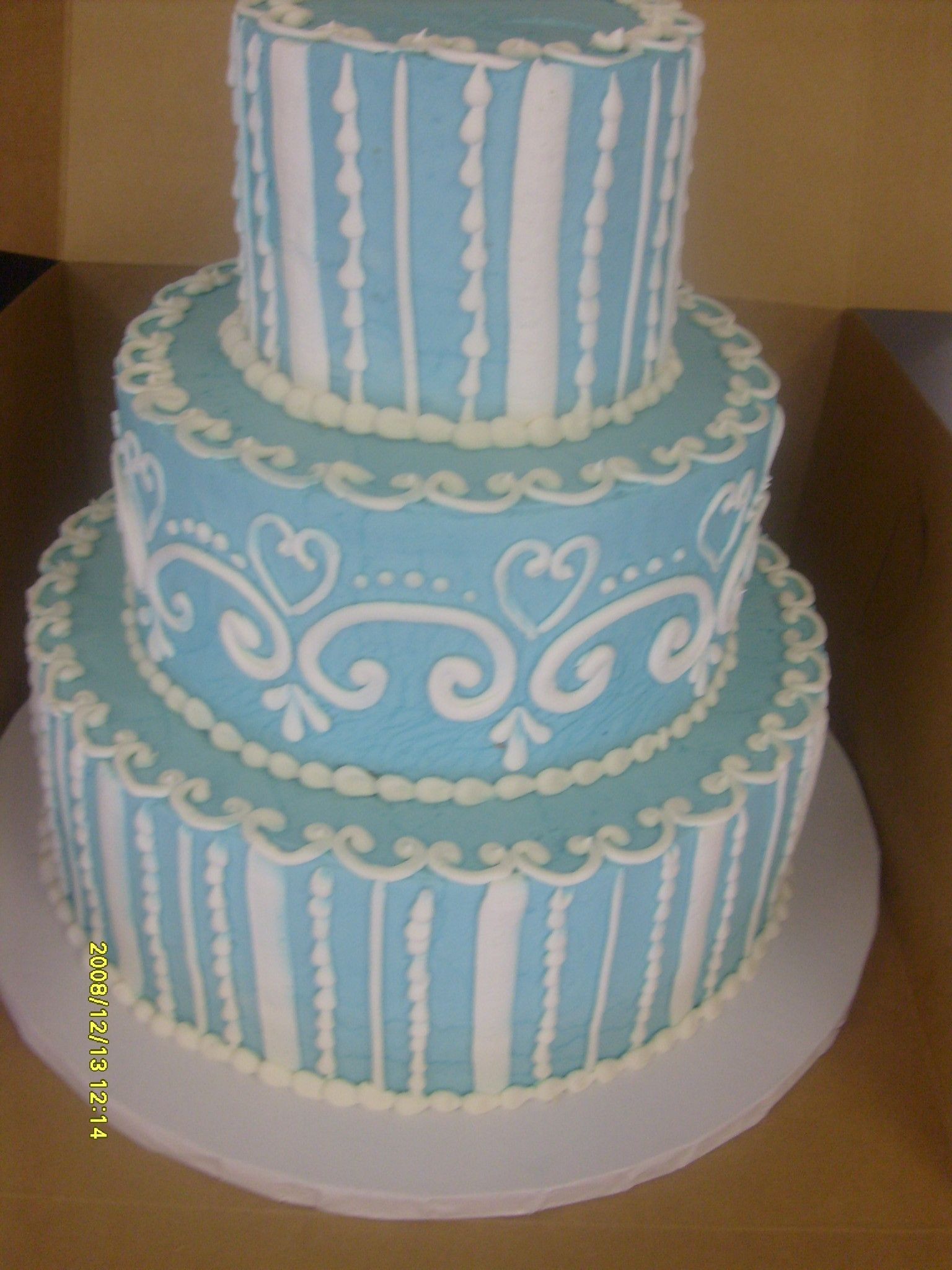 Three-tiered blue and white decorated cake on a white cake board