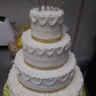 Four-tier white wedding cake with gold ribbon accents and scalloped icing decorations