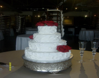White tiered wedding cake with red roses on a silver stand at a banquet table